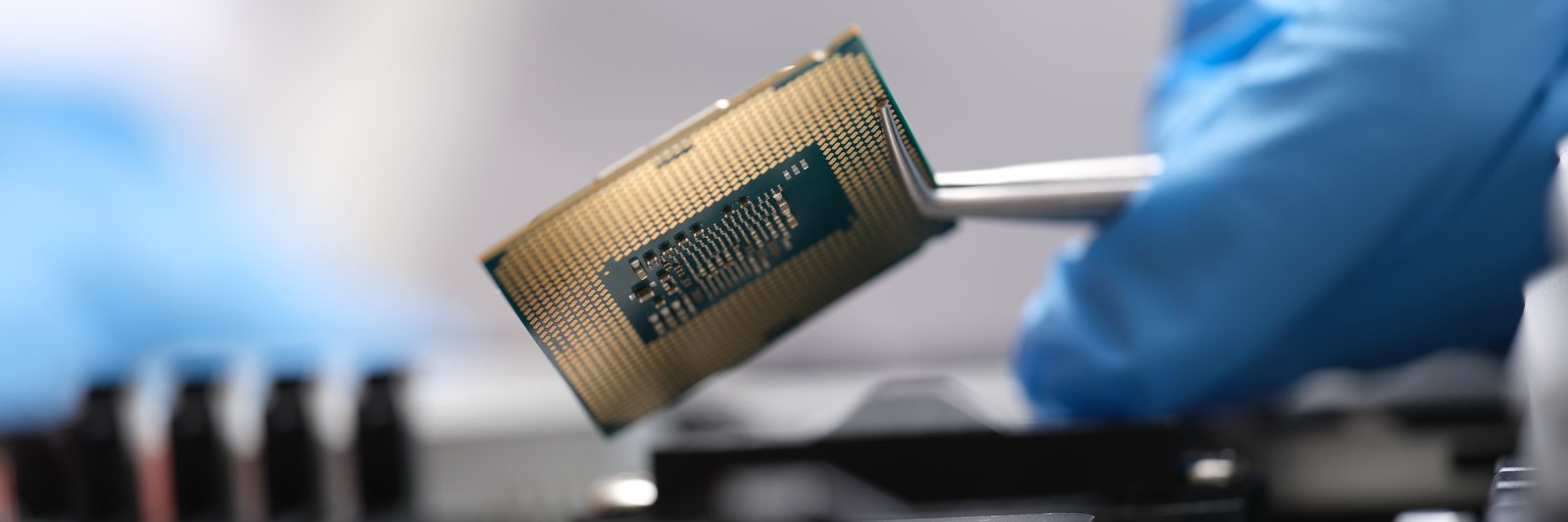 A processor held in tweezers above a circuit board, gold contact pins in focus.