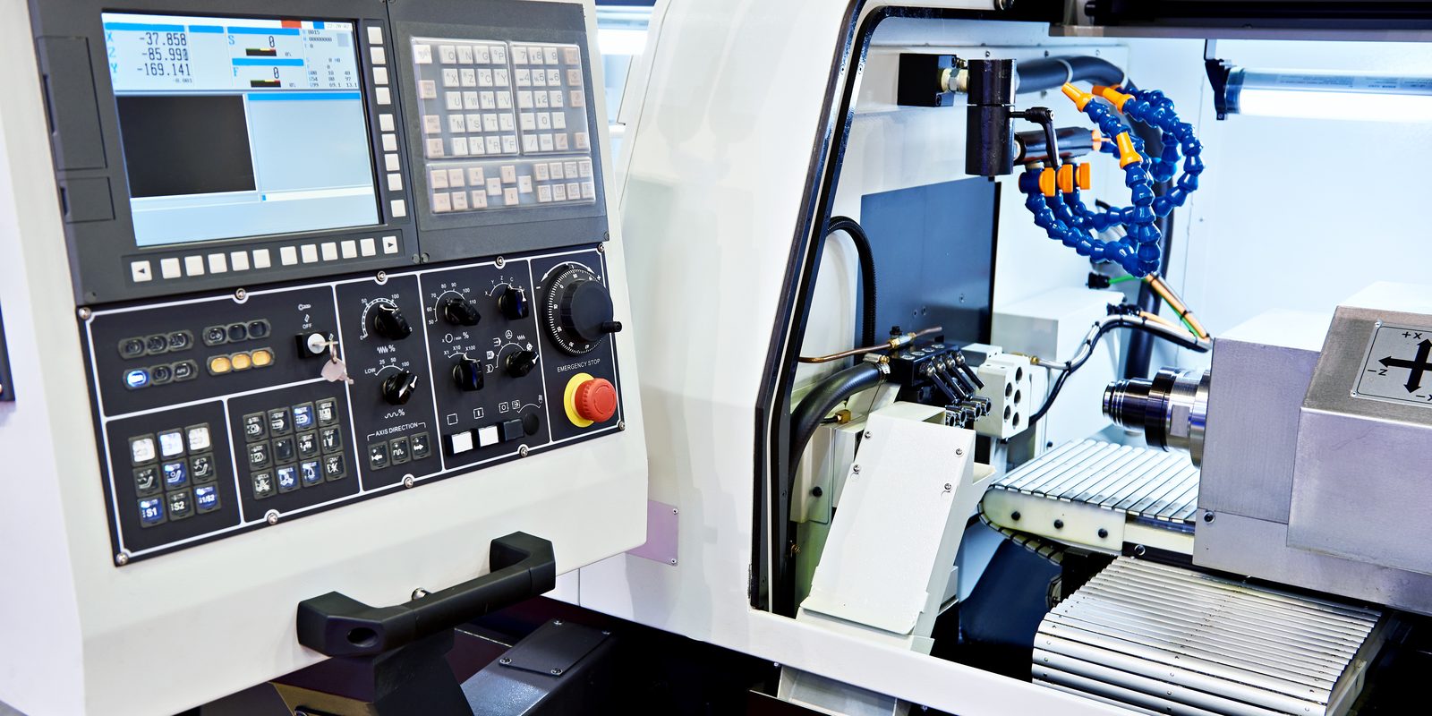A CNC turning centre with its control panel and tooling area, coolant lines in view.