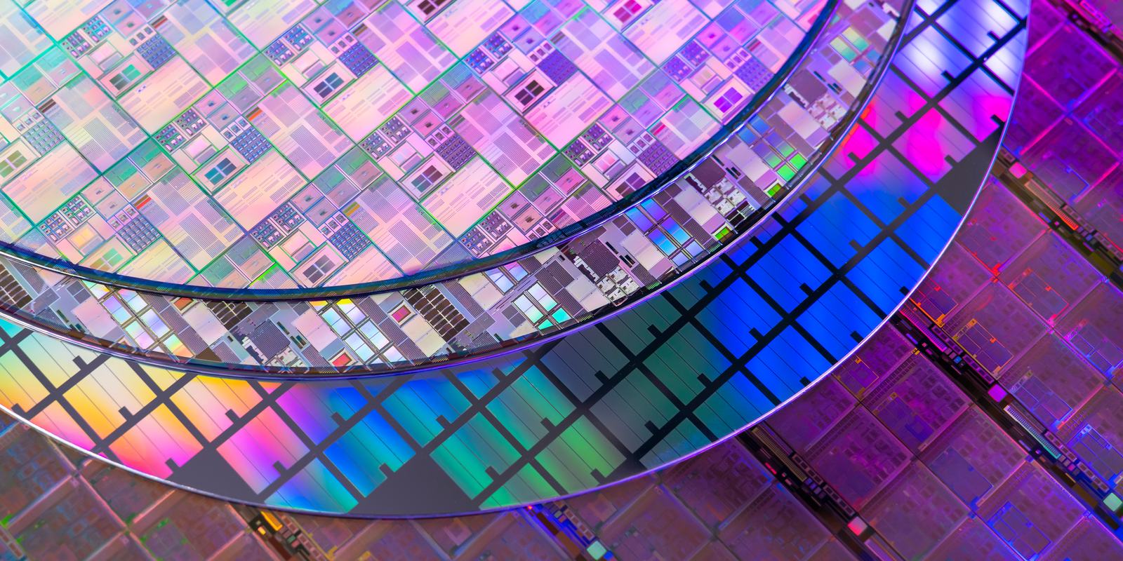 Patterned silicon wafers overlapping, their die grids showing diffraction colour.