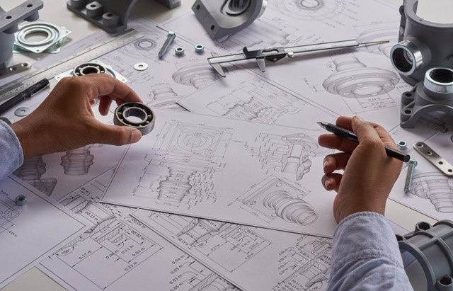 An engineer measuring a bearing with callipers over a set of technical drawings.