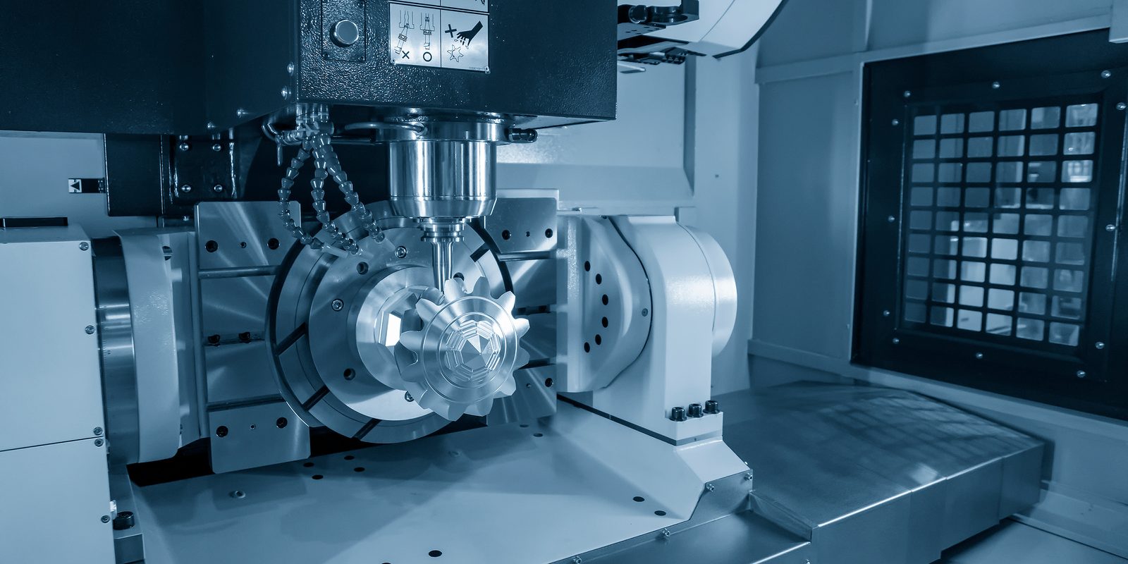 A five-axis machining centre cutting a precision part on a rotary trunnion.